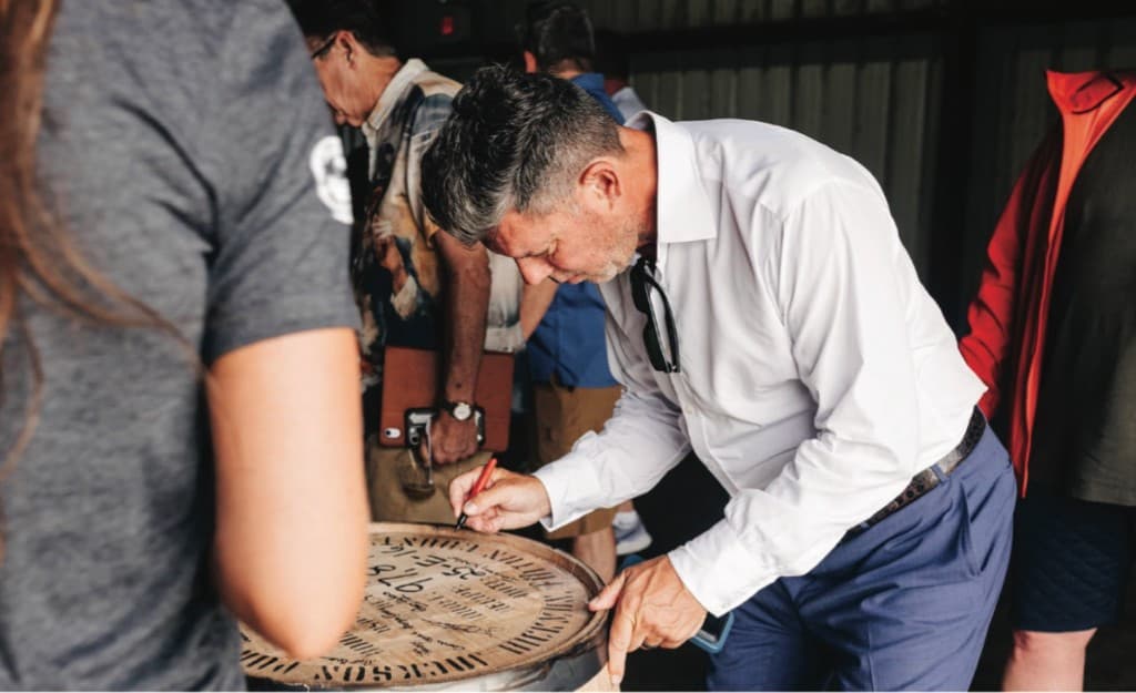 A barrel owner signing their barrel head at the distillery